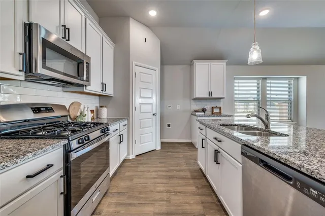 a large kitchen with stainless steel appliances granite countertop a stove top oven a sink dishwasher a microwave oven and a granite counter top