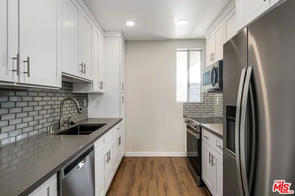 a kitchen with stainless steel appliances granite countertop a refrigerator a sink and white cabinets
