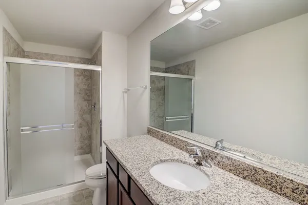 a bathroom with a granite countertop shower sink vanity and toilet
