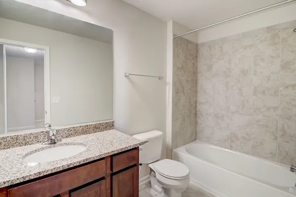 a bathroom with a granite countertop bathtub shower sink vanity mirror and toilet