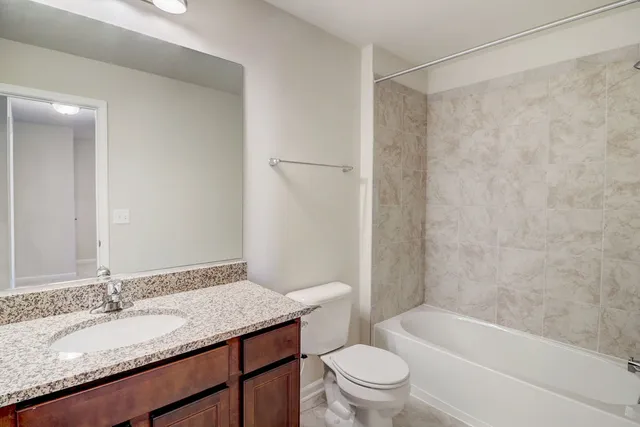 a bathroom with a granite countertop bathtub shower sink vanity mirror and toilet