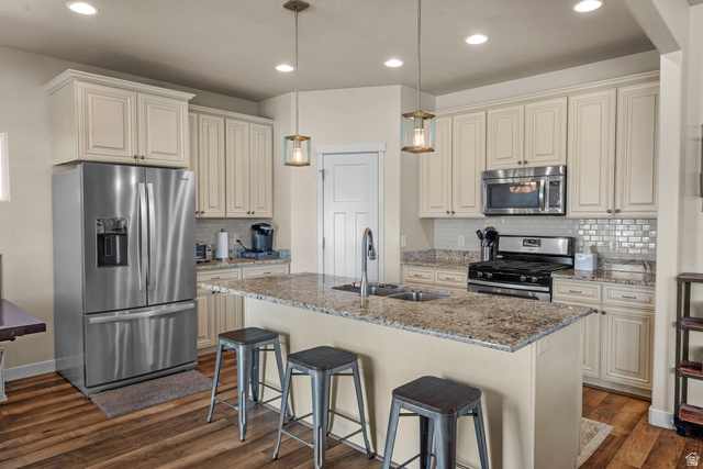 955 Delorean Lane Midvale, UT 84047 - Photo 14 of 47 Kitchen featuring a granite-topped island with seating, stainless steel appliances, extensive cabinetry, a tiled backsplash, and wood-finish flooring