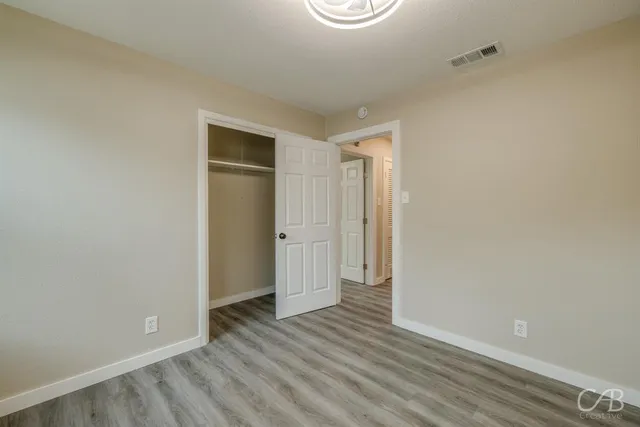a view of an empty room with wooden floor and closet