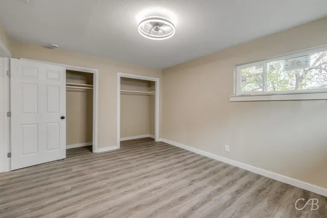 an empty room with wooden floor closet and windows