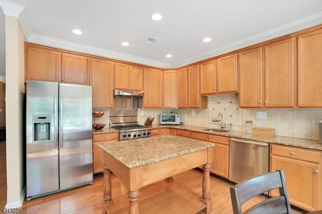 a kitchen with stainless steel appliances granite countertop a refrigerator a sink a stove a dining table and chairs