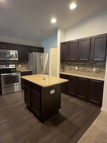 a kitchen with stainless steel appliances granite countertop wooden cabinets a sink a stove a microwave and island