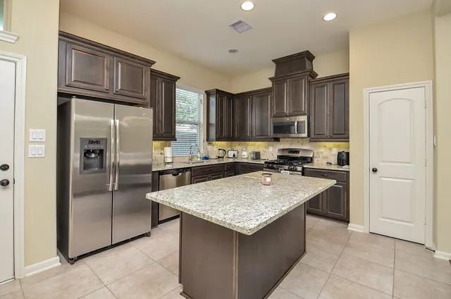 a kitchen with kitchen island granite countertop wooden cabinets a refrigerator and a sink