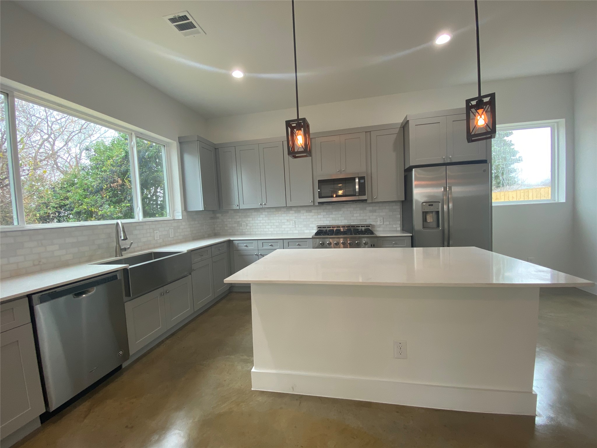 1916 Webberville Road, Unit B Austin, TX 78721 - Photo 6 of 25 Modern kitchen featuring light gray cabinetry, stainless steel appliances, white subway tile backsplash, a large center island with a white countertop, and concrete flooring