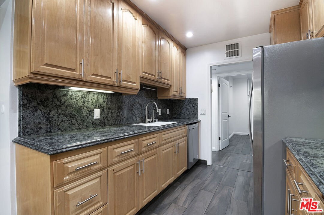 853 Le Doux Road, Unit 201 Los Angeles, CA 90035 - Photo 17 of 36 a kitchen with stainless steel appliances granite countertop a refrigerator a sink dishwasher and wooden cabinets with wooden floor