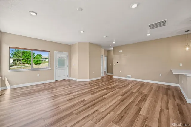 a view of an empty room with wooden floor and a window