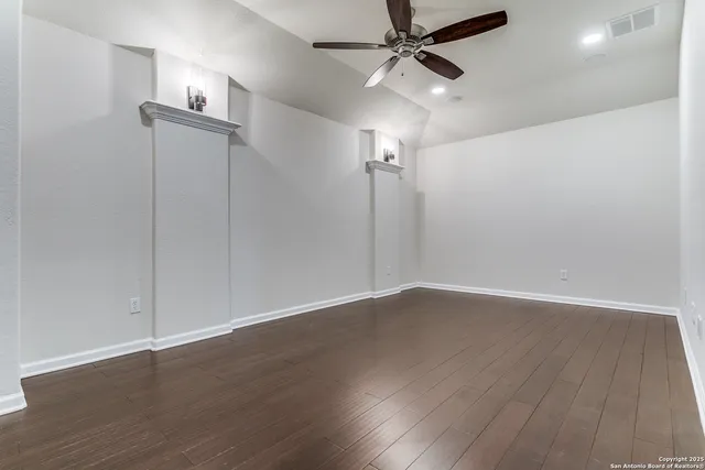 an empty room with wooden floor fan and windows