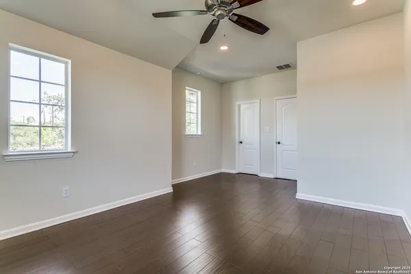 an empty room with wooden floor fan and windows