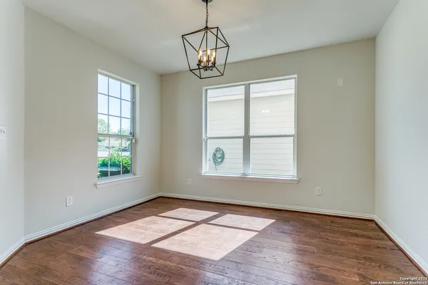 an empty room with wooden floor chandelier and windows