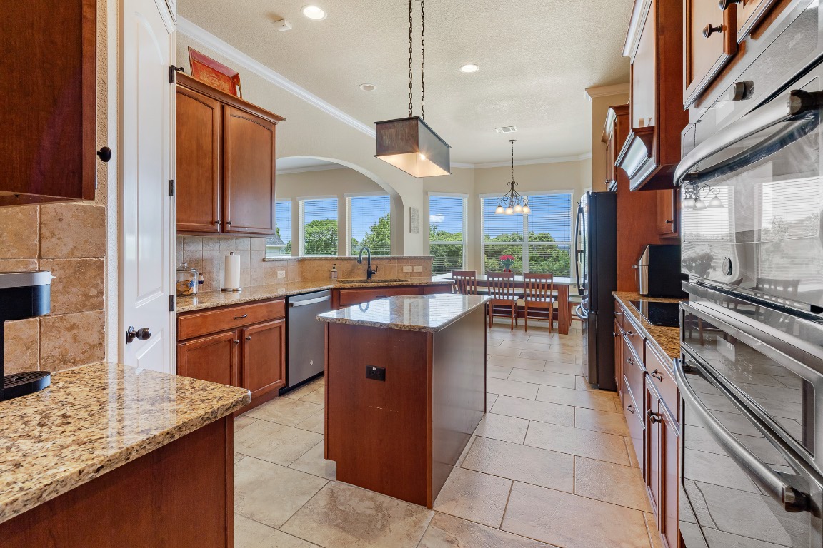 144 Indian Ridge Road Belton, TX 76513 - Photo 8 of 24 Kitchen featuring appliances with stainless steel finishes, crown molding, decorative backsplash, pendant lighting, and brown cabinetry
