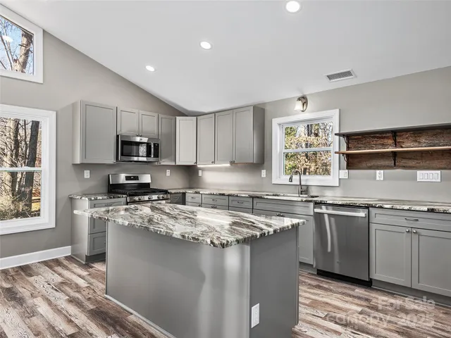 a kitchen with stainless steel appliances granite countertop a sink a stove a refrigerator cabinets and a window