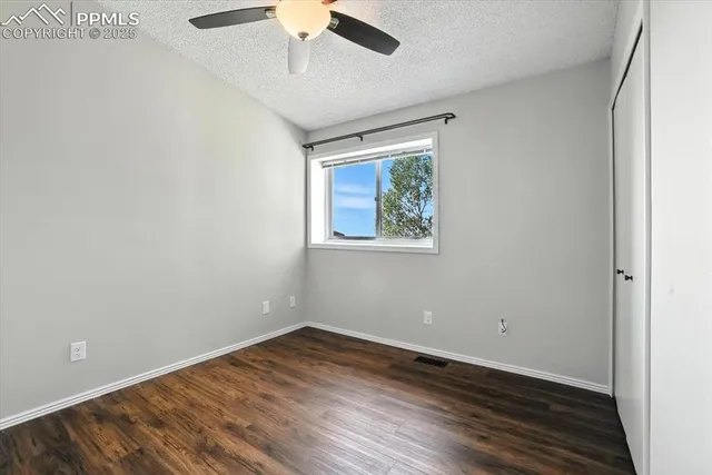 an empty room with wooden floor ceiling fan and windows