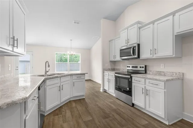 a kitchen with stainless steel appliances granite countertop white cabinets a sink dishwasher a stove and a refrigerator with wooden floor