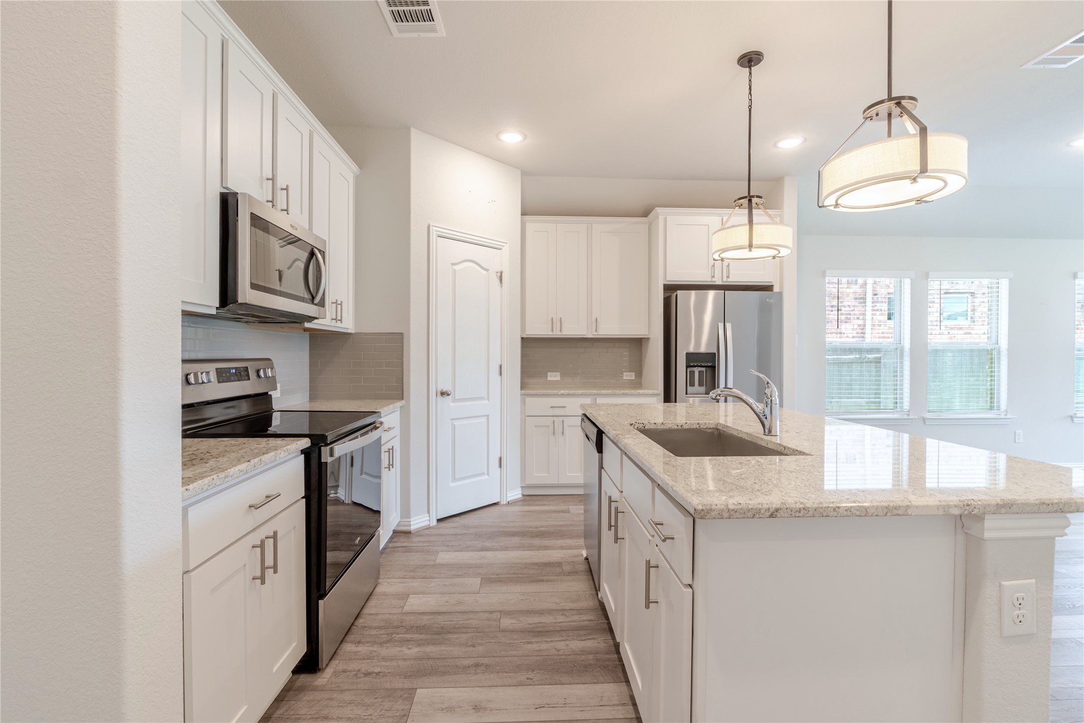 1117 Terrace View Georgetown, TX 78628 - Photo 15 of 25 Modern kitchen featuring an expansive center island with an undermount sink, pendant lighting, stainless steel appliances, and wood-finish flooring