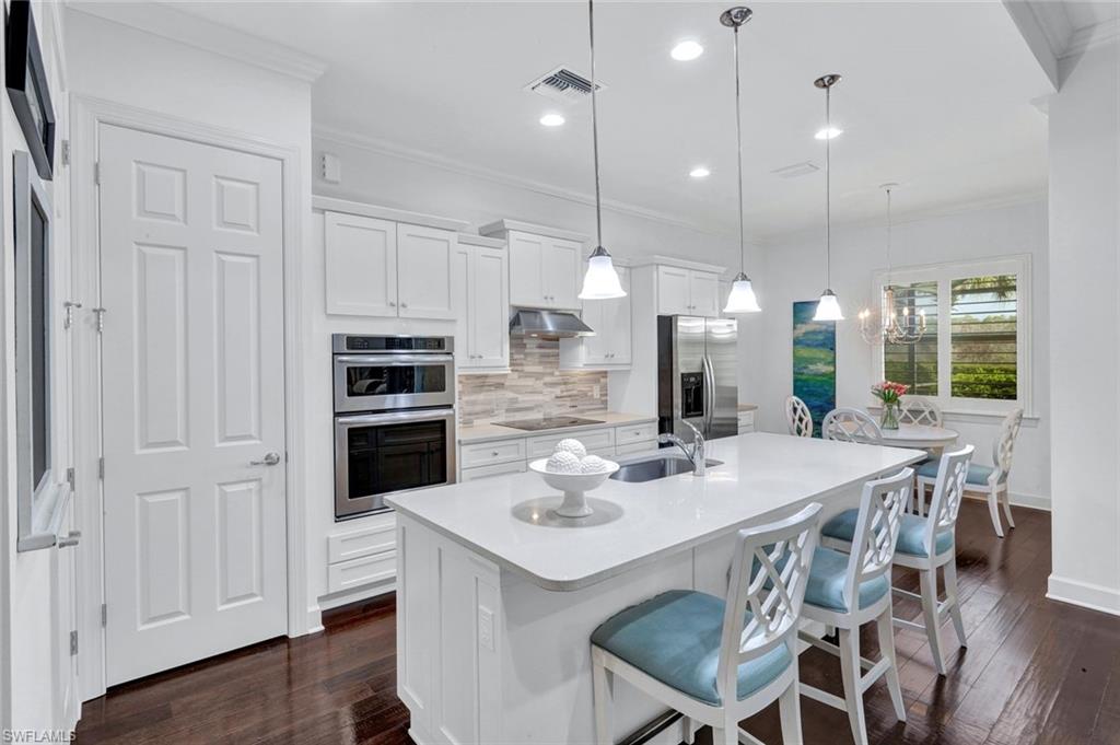 9311 Fieldstone Lane Naples, FL 34120 - Photo 6 of 48 a kitchen with stainless steel appliances kitchen island granite countertop a stove a refrigerator a kitchen island a dining table and chairs with wooden floor