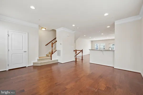 a view of an empty room with wooden floor kitchen view and a window