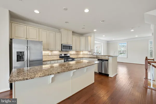 a kitchen with stainless steel appliances granite countertop a refrigerator a sink dishwasher a stove and white cabinets with wooden floor