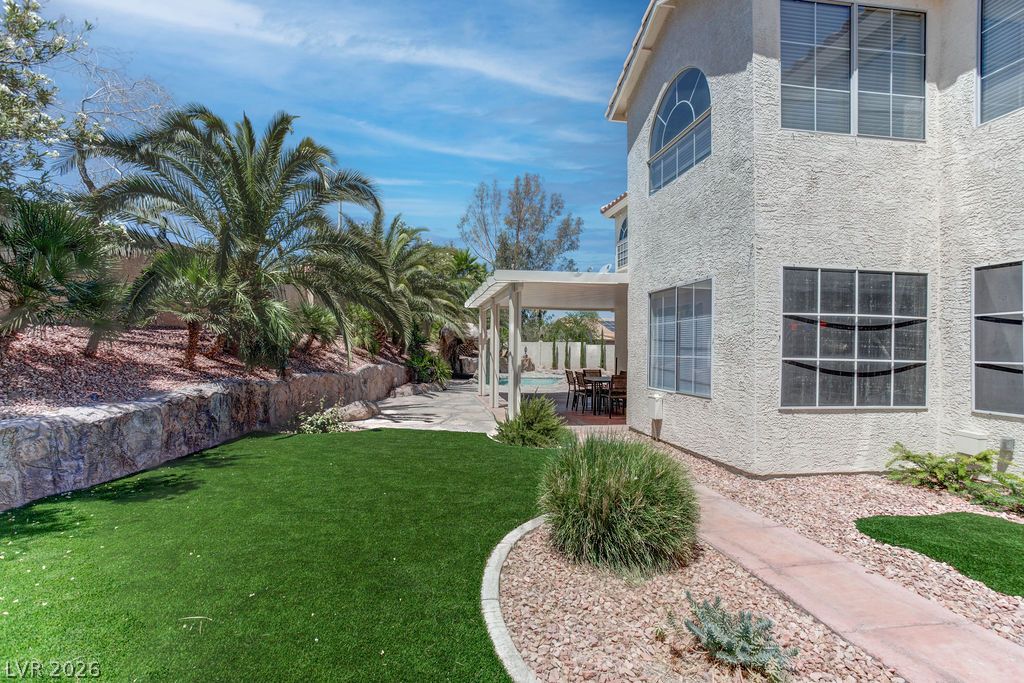 1 Rising Sun Court Henderson, NV 89074 - Photo 39 of 47 Palm trees fringe the manicured green lawn, leading to a covered patio with a pool beyond.