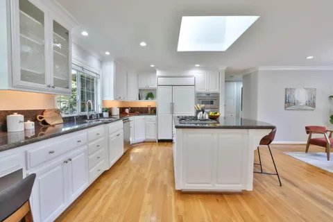 a kitchen with stainless steel appliances granite countertop a stove a sink a refrigerator and white cabinets with wooden floor