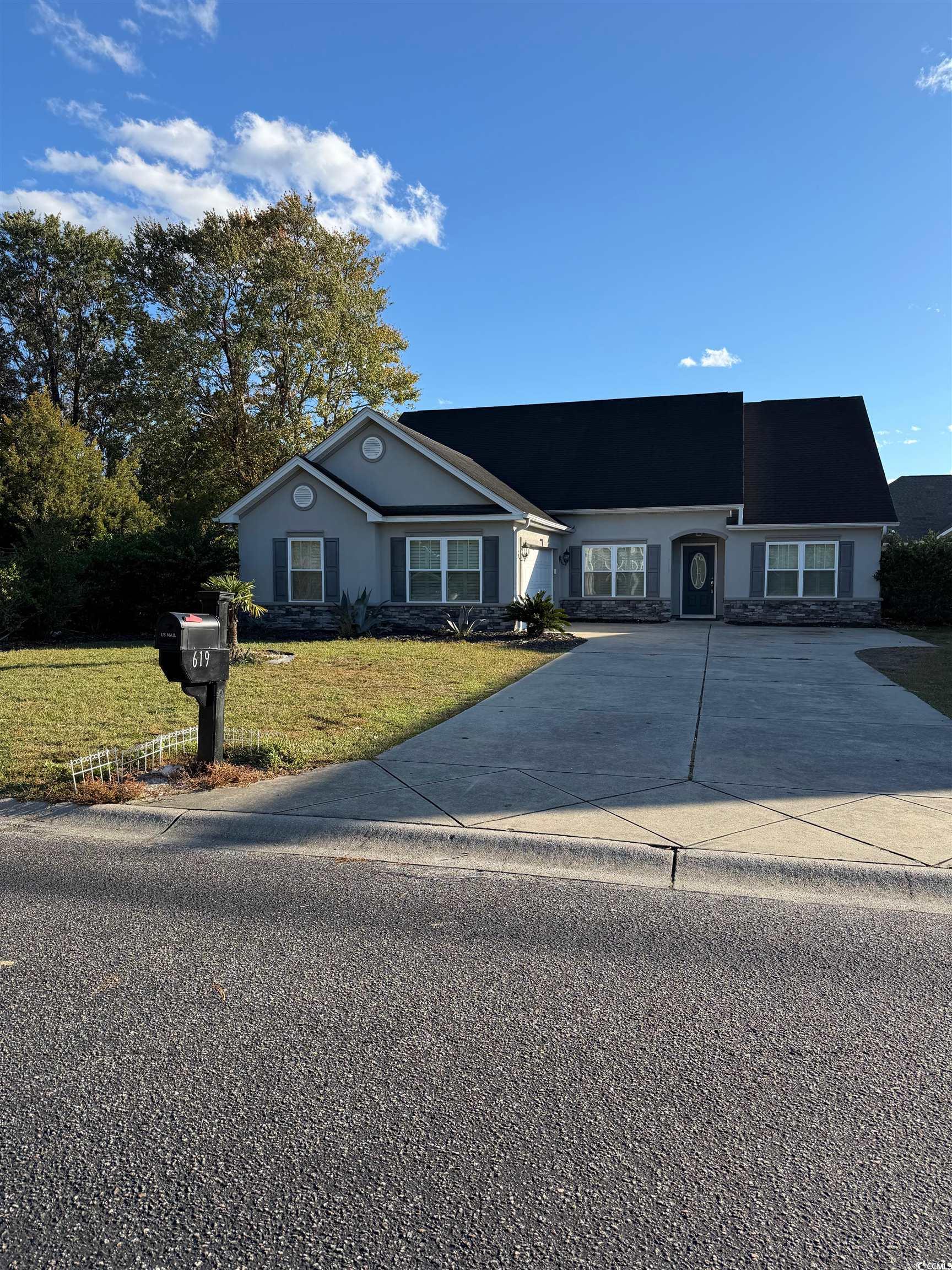 Ranch-style house featuring a front yard, stone siding, driveway, and stucco siding