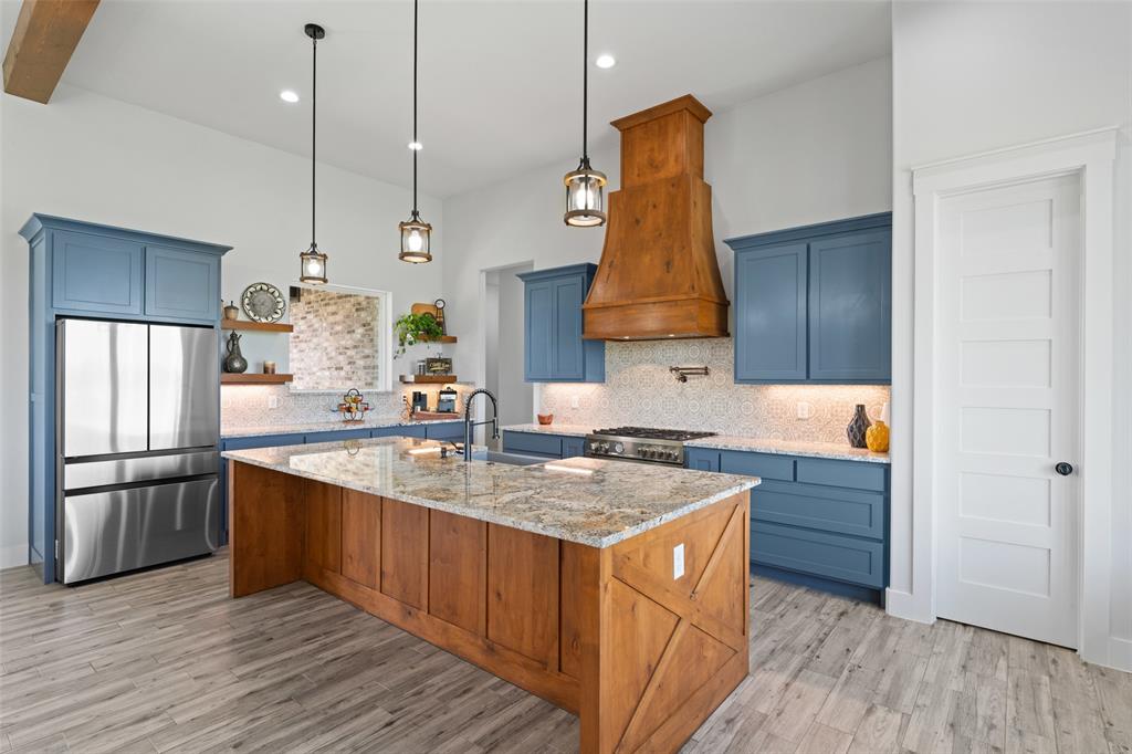 4411 Fm 751 Wills Point Wills Point, TX 75169 - Photo 16 of 40 Spacious kitchen featuring a large wood-finish island with a stone-finish countertop, blue cabinetry, a wood-finish range hood, stainless steel appliances, and light wood-finish flooring