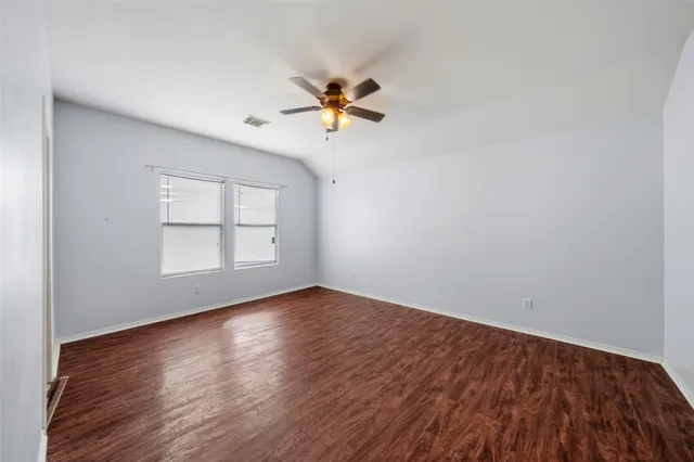 an empty room with wooden floor chandelier fan and windows