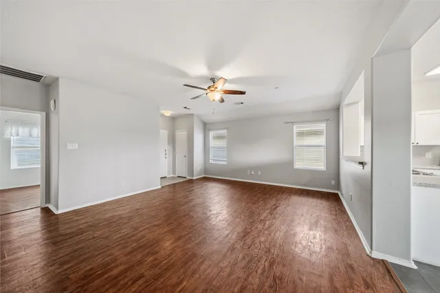 an empty room with wooden floor chandelier fan and windows