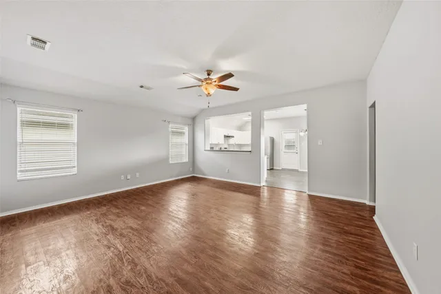 an empty room with fan and a kitchen view