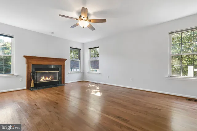 a view of an empty room with wooden floor fireplace and a window