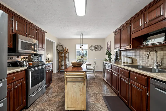 a kitchen with stainless steel appliances granite countertop a stove top oven a sink dishwasher a dining table and chairs with wooden cabinets