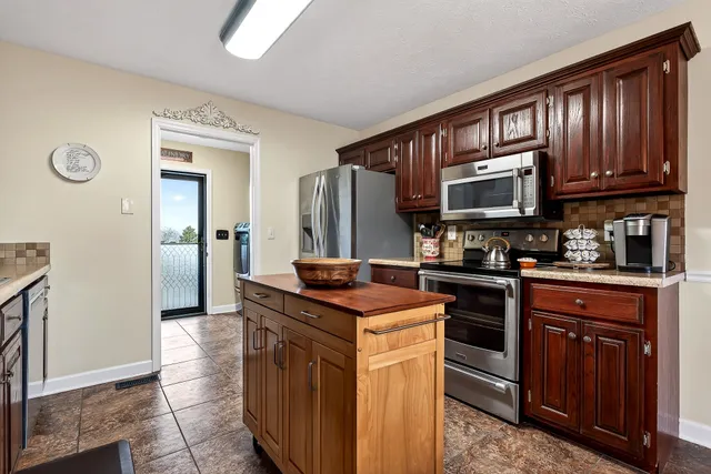 a kitchen with stainless steel appliances granite countertop a stove top oven a sink dishwasher and a refrigerator with wooden cabinets