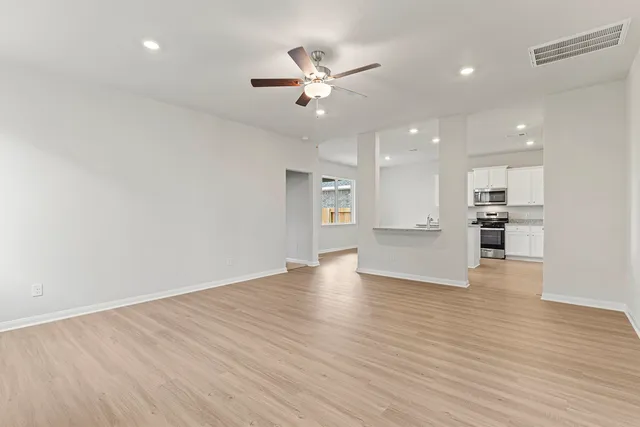 a view of an empty room with wooden floor and a ceiling fan