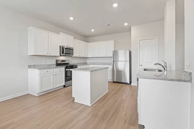 a kitchen with stainless steel appliances granite countertop white cabinets a sink a stove a refrigerator and a microwave oven with wooden floor