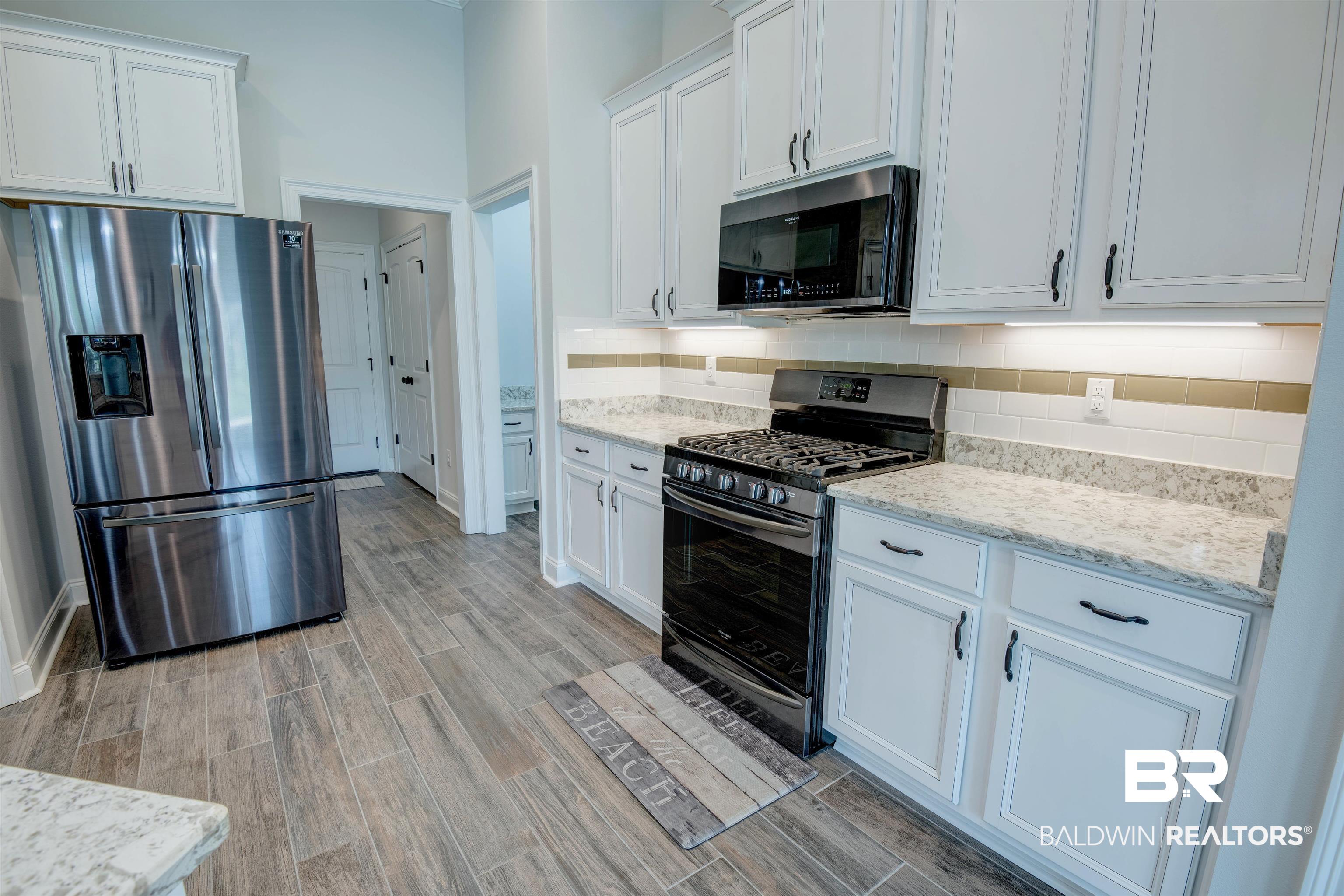 9843 Chipper Lane Foley, AL 36535 - Photo 9 of 34 Kitchen featuring stainless steel appliances, light wood-type flooring, decorative backsplash, and white cabinetry