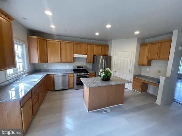 a kitchen with stainless steel appliances kitchen island granite countertop a stove a sink a refrigerator white cabinets and couches with wooden floor