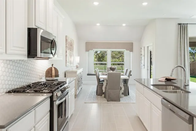 a kitchen with stainless steel appliances granite countertop a stove top oven a sink dishwasher a dining table and chairs with wooden floor