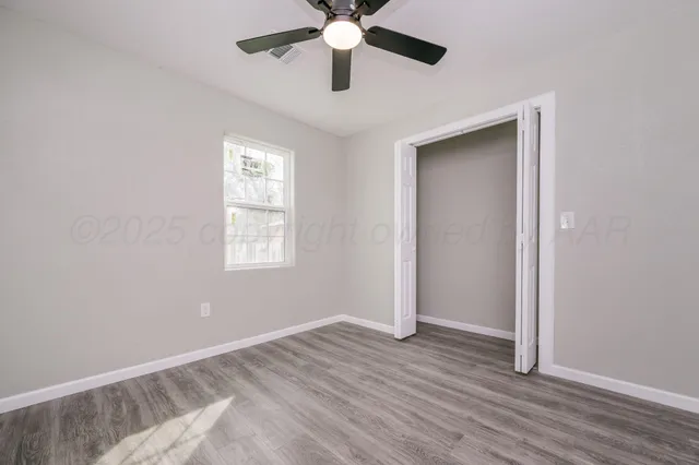 a view of an empty room with wooden floor and a ceiling fan