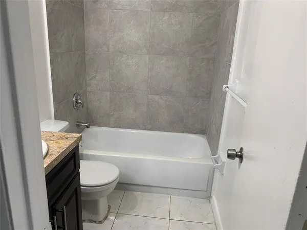 a bathroom with a granite countertop bathtub shower sink vanity and toilet