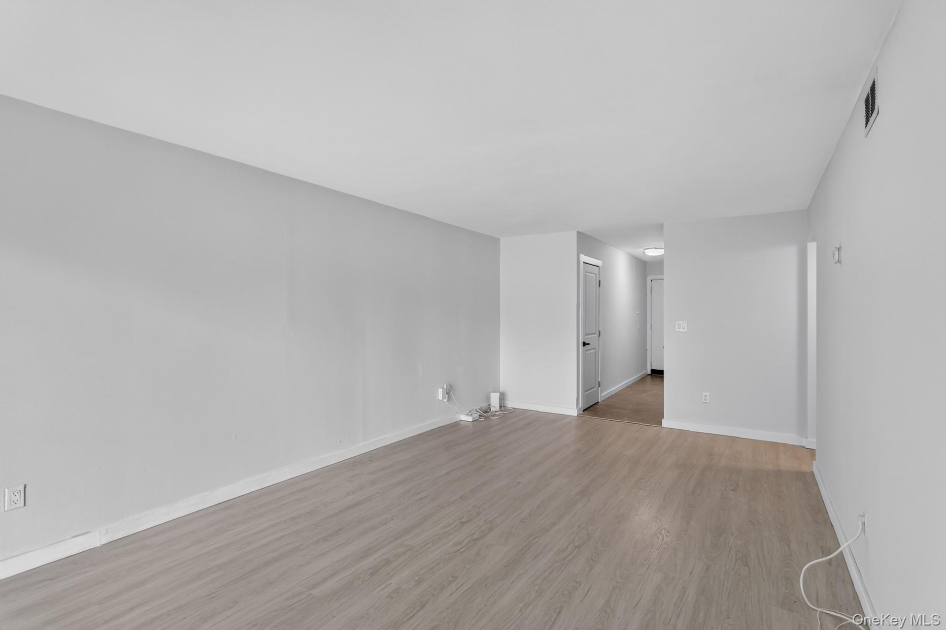 26 Cooper Road, Unit 414 Poughkeepsie, NY 12603 - Photo 7 of 24 Spacious room featuring light wood-finish flooring, light gray walls, white baseboards, a flat white ceiling, and a hallway with white doors