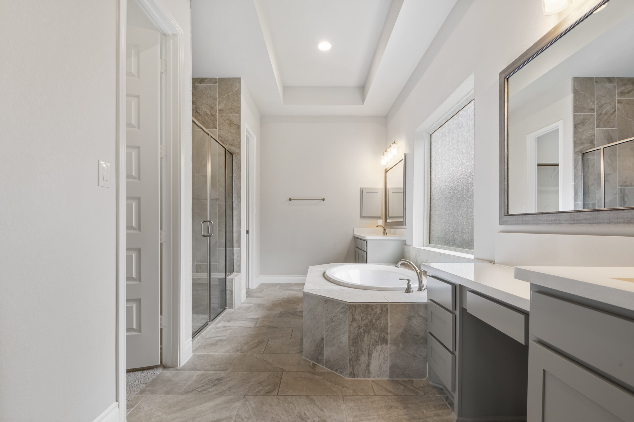 104 Catani Loop Georgetown, TX 78628 - Photo 9 of 34 Well-appointed bathroom featuring a built-in tub with tile surround, a glass-enclosed shower, dual vanities, and a window with privacy glass