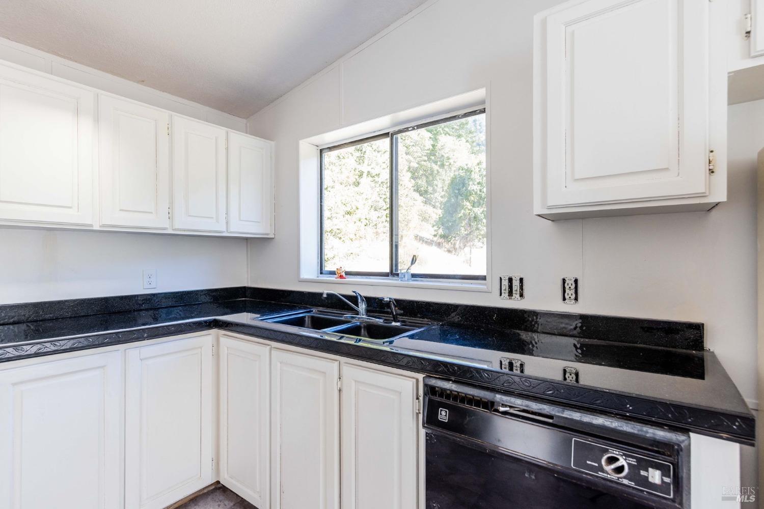 a kitchen with granite countertop white cabinets sink and window