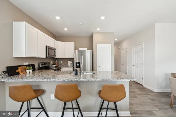 a kitchen with stainless steel appliances granite countertop a refrigerator a stove a sink a dining table and chairs with wooden floor