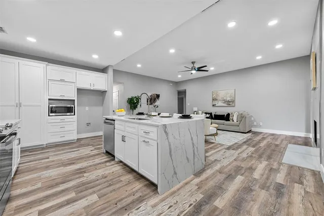 a large white kitchen with kitchen island a sink a center island and stainless steel appliances