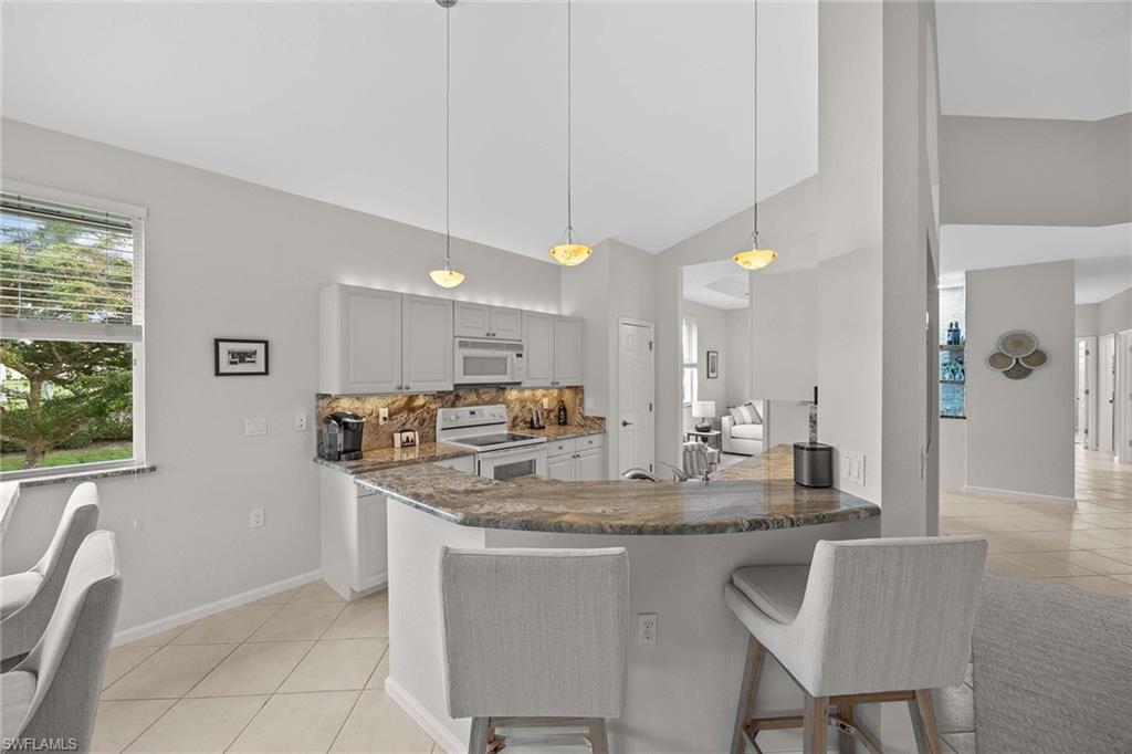 6864 Ascot Drive, Unit 5202 Naples, FL 34113 - Photo 11 of 36 a kitchen with stainless steel appliances granite countertop a sink a stove a dining table and chairs