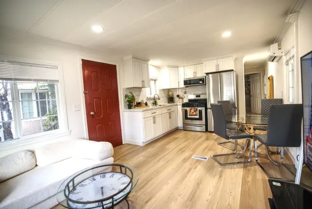 a open kitchen with stainless steel appliances granite countertop a refrigerator a stove a sink dishwasher a dining table and chairs with wooden floor