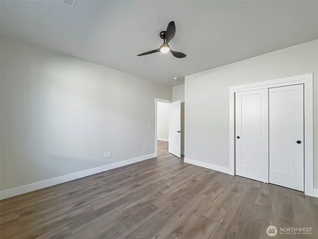a view of an empty room with wooden floor and a ceiling fan
